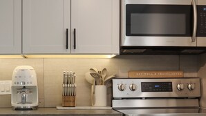 Une cuisine moderne équipée d’appareils électroménagers en acier inoxydable, notamment une machine à café, un four à micro-ondes et un four traditionnel. Une pancarte en bois fixée au four porte l’inscription suivante : « MANGEZ BIEN ET VOYAGEZ SOUVENT ».