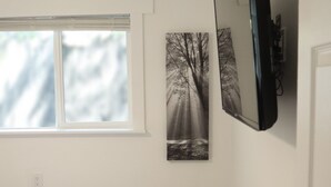 Une chambre à coucher avec un lit, une fenêtre, un téléviseur fixé au mur et deux tableaux encadrés.
