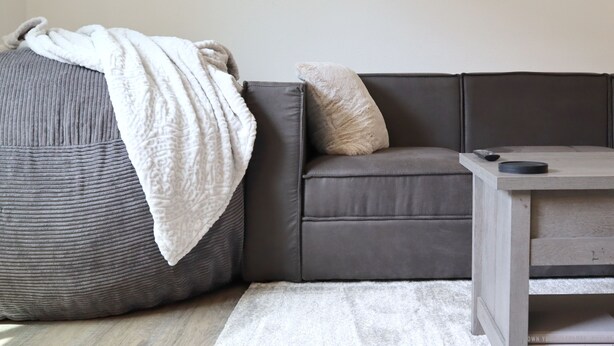Un salon moderne avec un canapé gris, un grand pouf, une petite table et une carte du monde accrochée au mur.