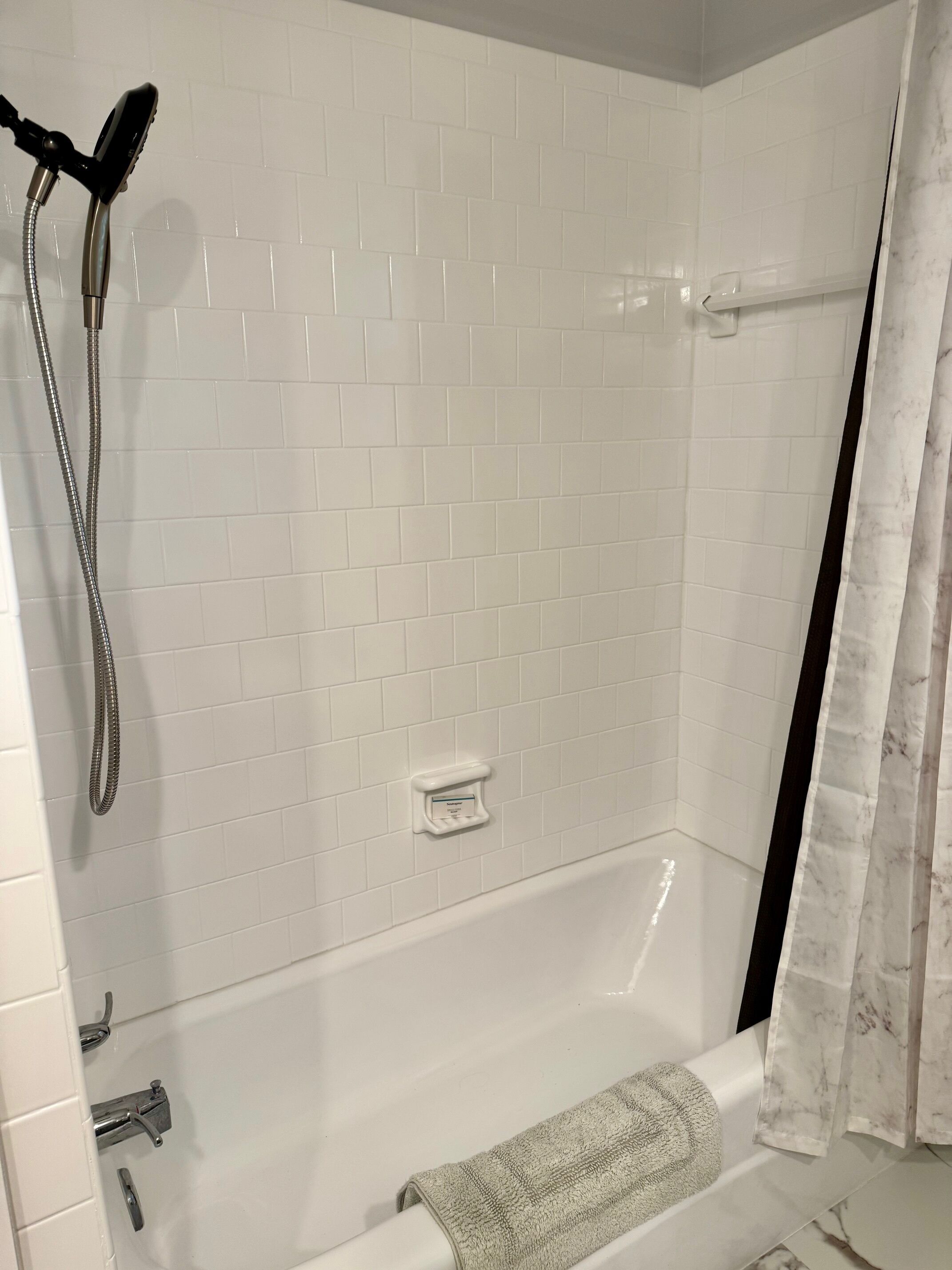 A bathroom with a white tiled shower enclosure, a handheld showerhead, a built-in soap dish, and a towel rack with a towel.