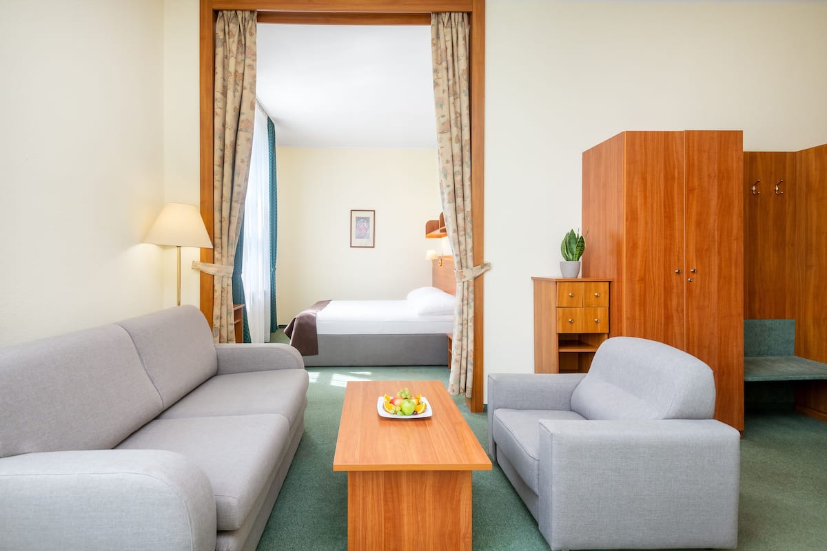 Et hotelværelse med sofa, lænestol, sofabord i træ og en seng med et natbord.