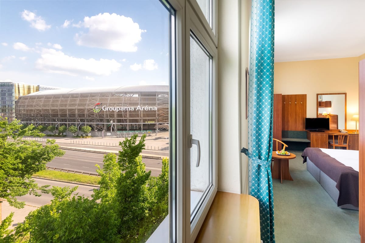 Et hotelværelse med udsigt til Groupama Arena, et moderne sportsstadion, og et spiseområde med et bord og stole.