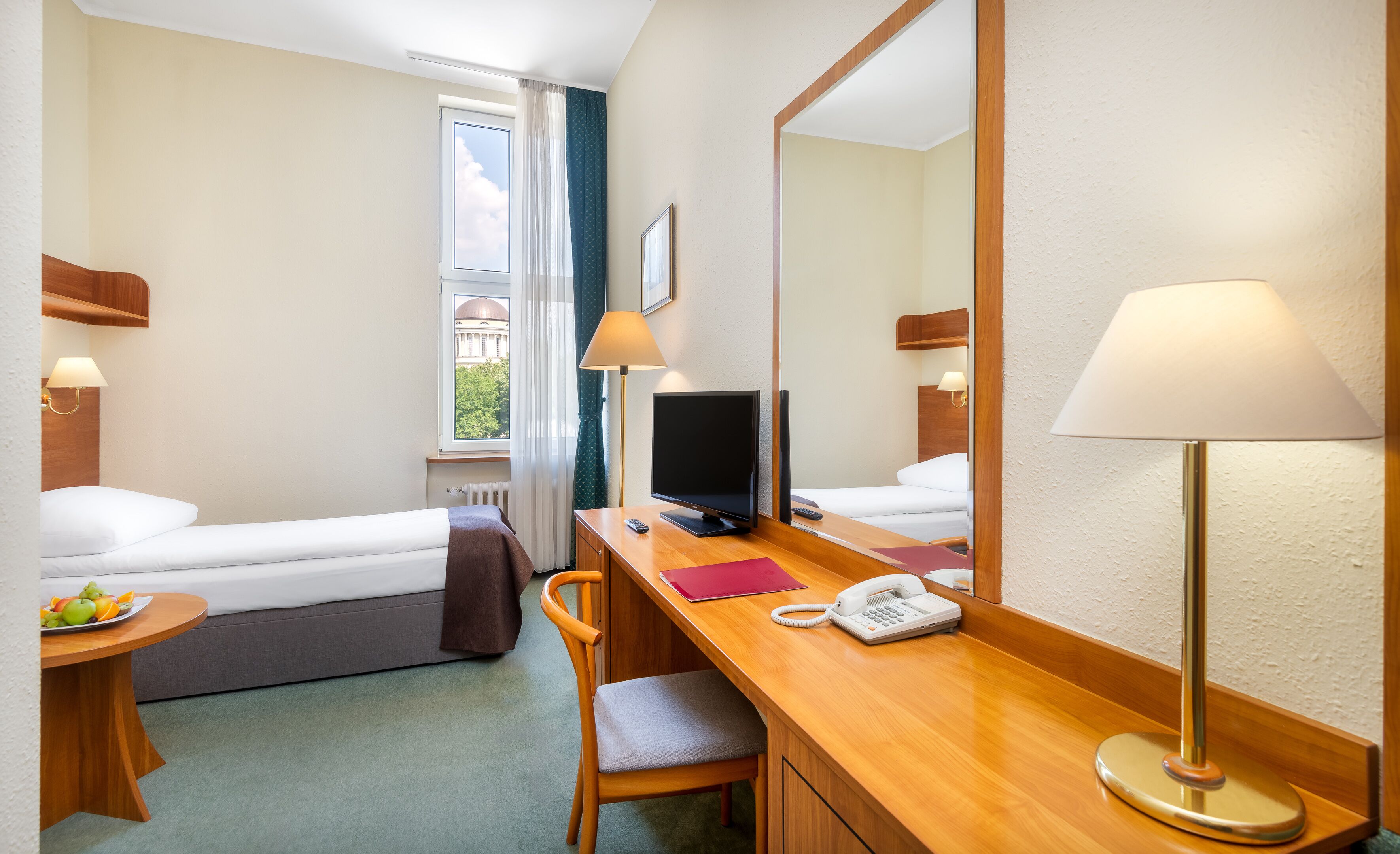 Ein Hotelzimmer mit Bett, Schreibtisch, Stuhl und einem großen Spiegel.