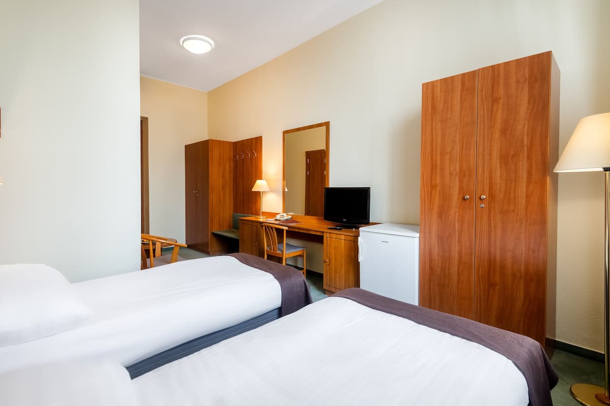 Et hotelværelse med to senge, et skrivebord med en computer, et fjernsyn og et klædeskab.