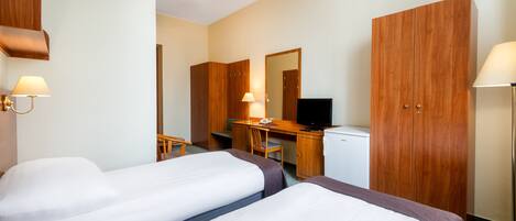 Quarto de hotel com duas camas, uma escrivaninha com computador, televisão e guarda-roupa.