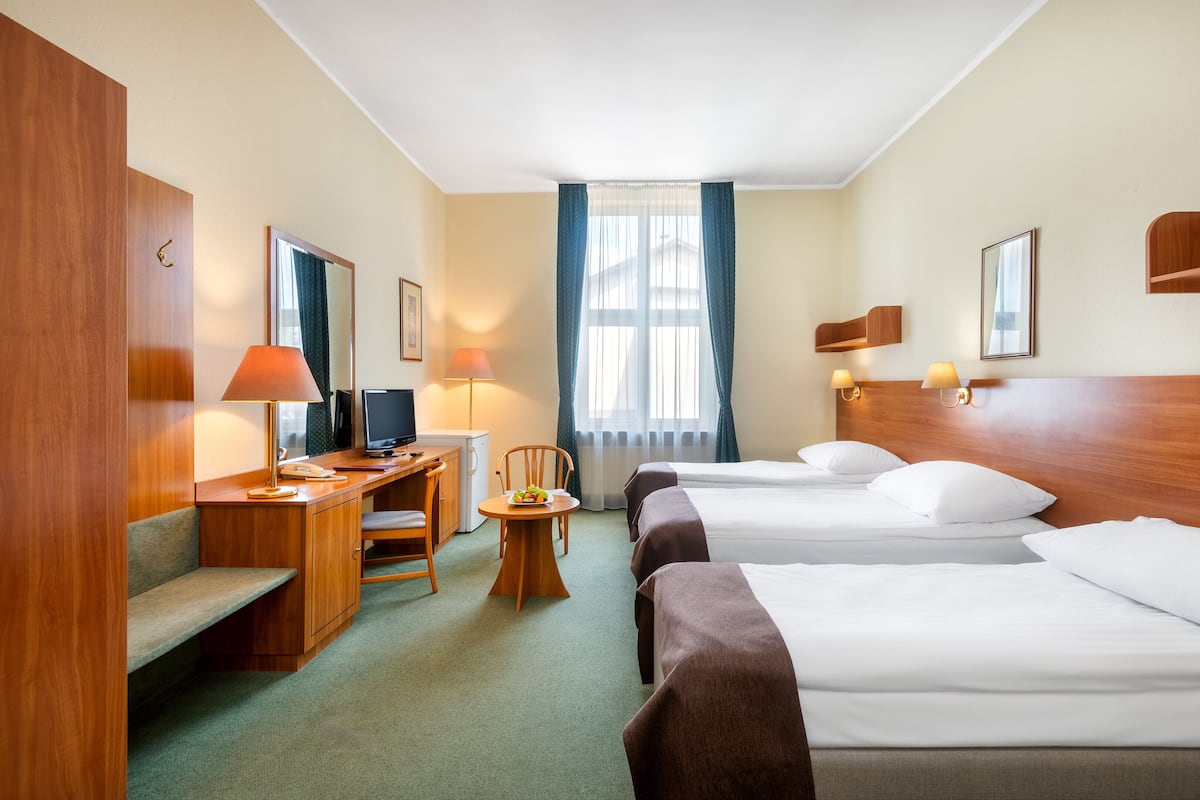 Et hotelværelse med et skrivebord, to senge, en stol, et lille bord med frugt og et fjernsyn.