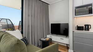 Uma sala de estar moderna com televisão de tela plana, um sofá, uma pequena mesa lateral e uma área de cozinha com micro-ondas.