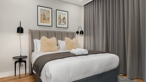 Quarto moderno com uma cama grande, duas fotos emolduradas na parede e uma cortina cinza.