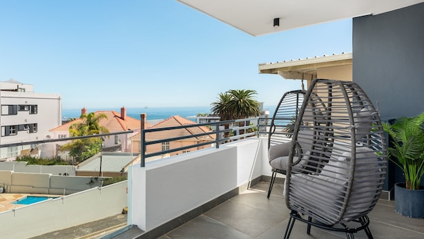 Uma varanda com vista para o mar, uma cadeira de vime e um vaso com planta.