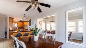 A dining area with a wooden table, chairs, a ceiling fan, and a kitchen in the background.