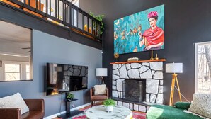 A living room with a fireplace, a large painting, a TV, and a staircase.