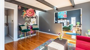 A modern living room with a wooden floor, a green chair, a red sofa, and a painting on the wall.
