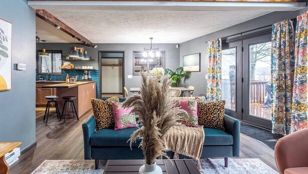 A living room with a sofa, a coffee table, and a decorative plant. There is a kitchen area with bar stools and a dining table. A staircase leads to an upper level. - Water Front Dream | Hot Tub | Fire Pit | King Bed | Community Pool | Basketball (Tobyhanna)