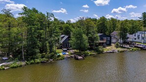 A lakeside property with multiple houses, a dock, and a small boat. - Water Front Dream | Hot Tub | Fire Pit | King Bed | Community Pool | Basketball (Tobyhanna)