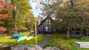 A cabin with a wooden deck, kayaks, and a stone pathway leading to it. - Water Front Dream | Hot Tub | Fire Pit | King Bed | Community Pool | Basketball (Tobyhanna)