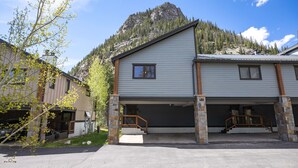 A two-story building with a garage, stone pillars, and a mountain backdrop.