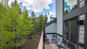 A wooden deck with two chairs, a view of a forest, and a building with large windows.
