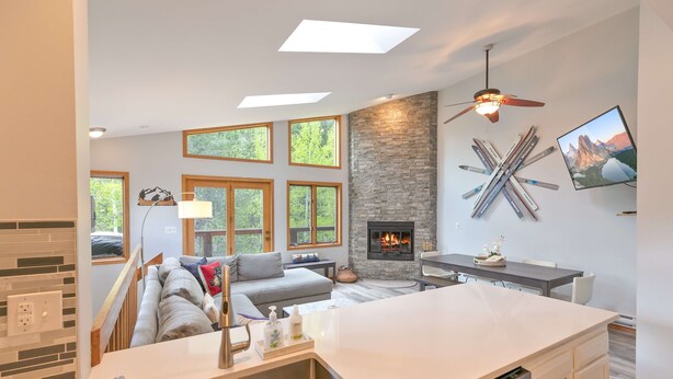 A modern living room with a fireplace, large windows, and a kitchen area.