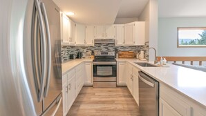 A modern kitchen with stainless steel appliances, white cabinetry, and a tiled backsplash.