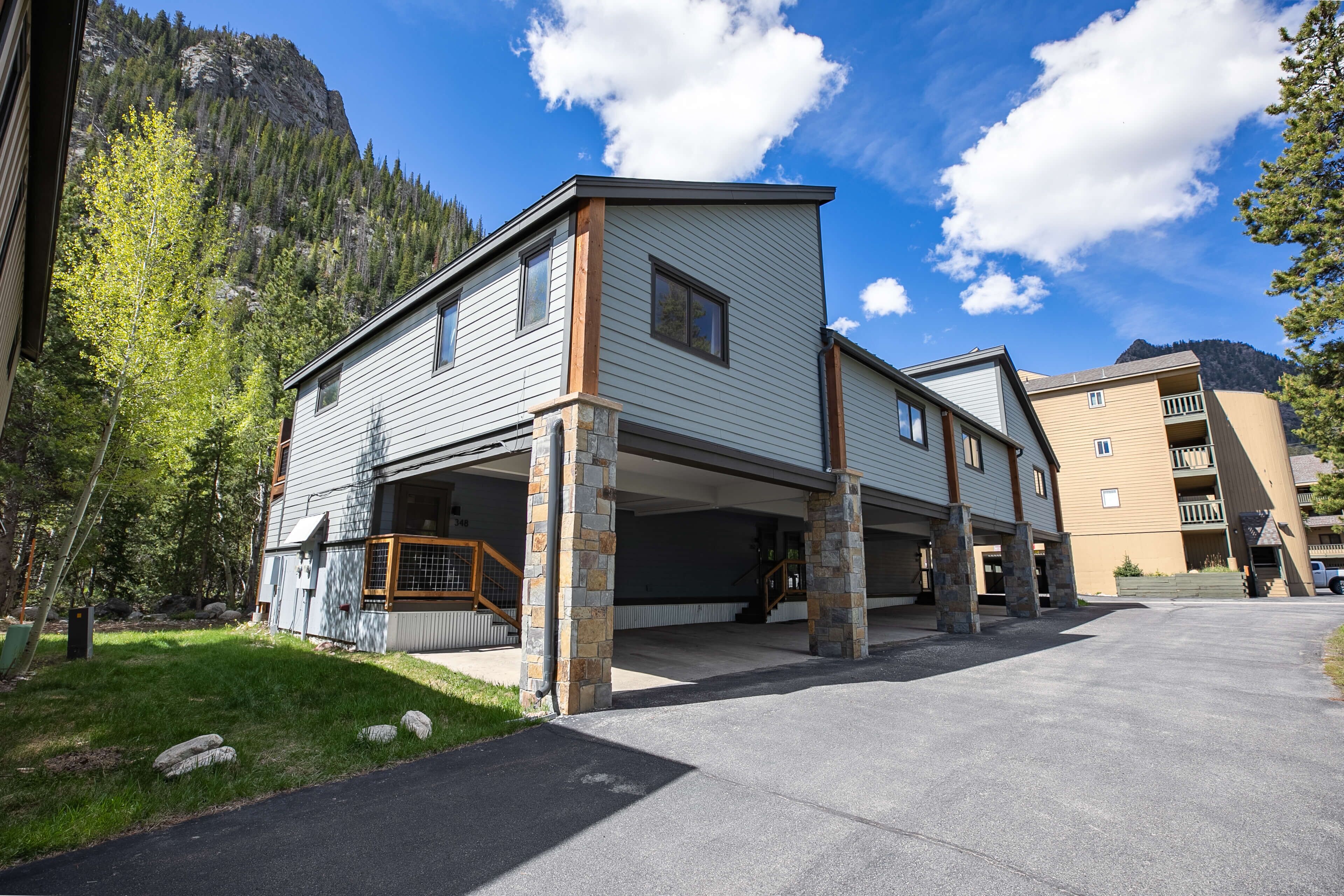 A multi-story building with a covered parking area, stone pillars, and a mountainous backdrop.
