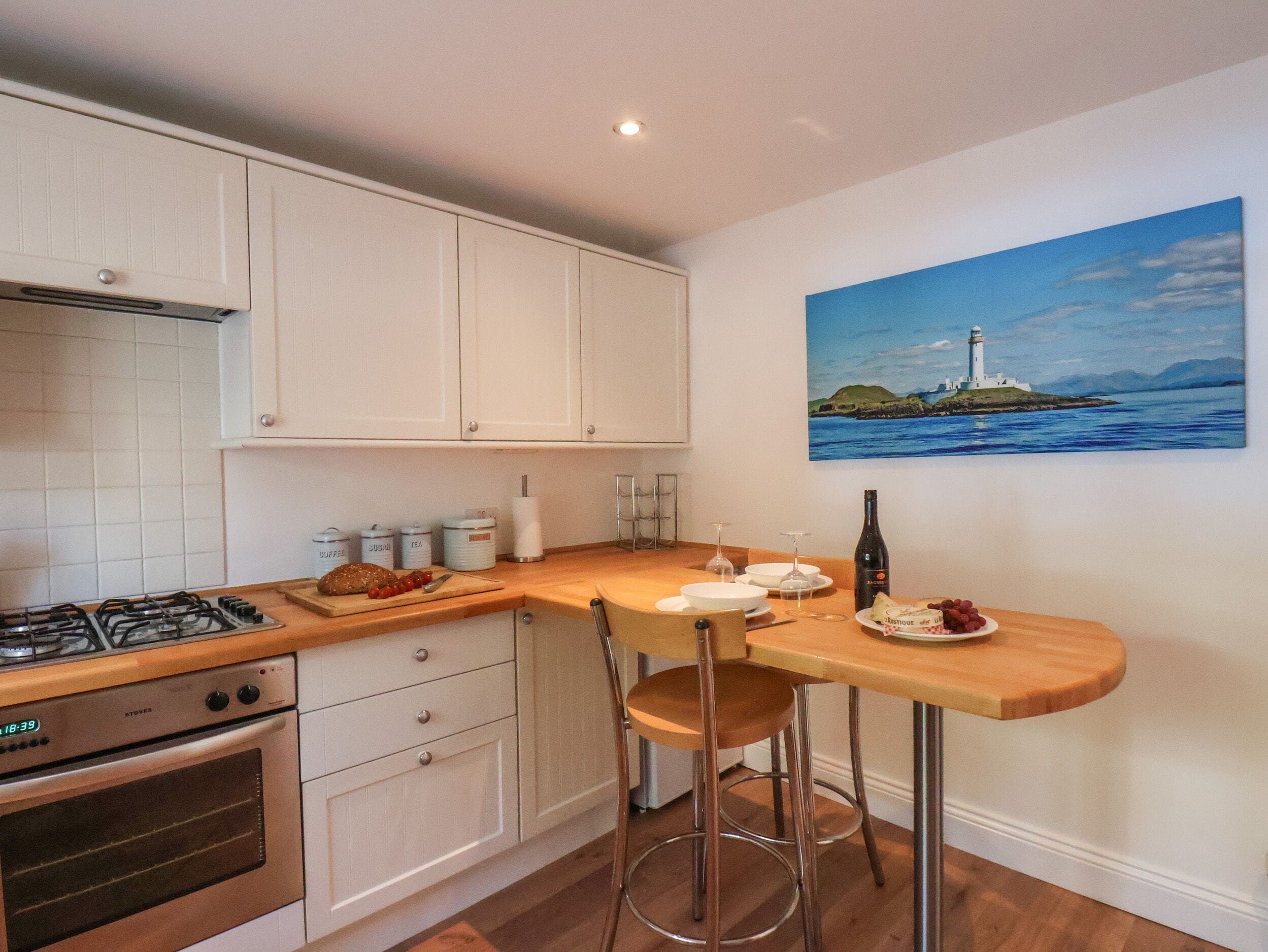 A kitchen with white cabinets, a wooden countertop, a gas stove, an oven, and a painting of a lighthouse on the wall.