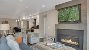 Een moderne woonkamer met een flatscreen televisie, een open haard en comfortabele zitplaatsen.