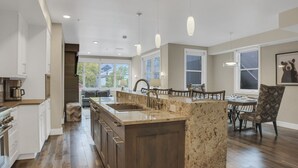 Een ruime keuken met een groot eiland, houten kastjes, en een eethoek met een tafel en stoelen.