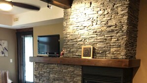 A stone fireplace with a television above it, a framed picture on the mantel, and a chair in the foreground. - 4-Bedroom Condo in Radium, BC (Radium Hot Springs)