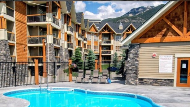 A pool area with a wooden deck, a stone wall, and a sign indicating a room number. - 4-Bedroom Condo in Radium, BC (Radium Hot Springs)