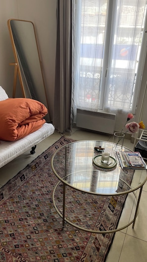 Un salon comprenant un canapé, une table basse en verre, un tapis à motifs, un grand miroir et une vue par la fenêtre.