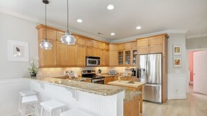 A modern kitchen with wooden cabinets, stainless steel appliances, and a granite countertop island with bar stools. - Pie Seas - 4 bedroom with elevator, dog friendly! (Carolina Beach)