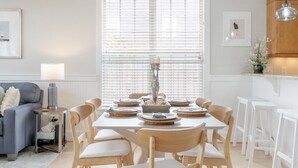 A modern dining area with a white table set for six, surrounded by wooden chairs. - Pie Seas - 4 bedroom with elevator, dog friendly! (Carolina Beach)