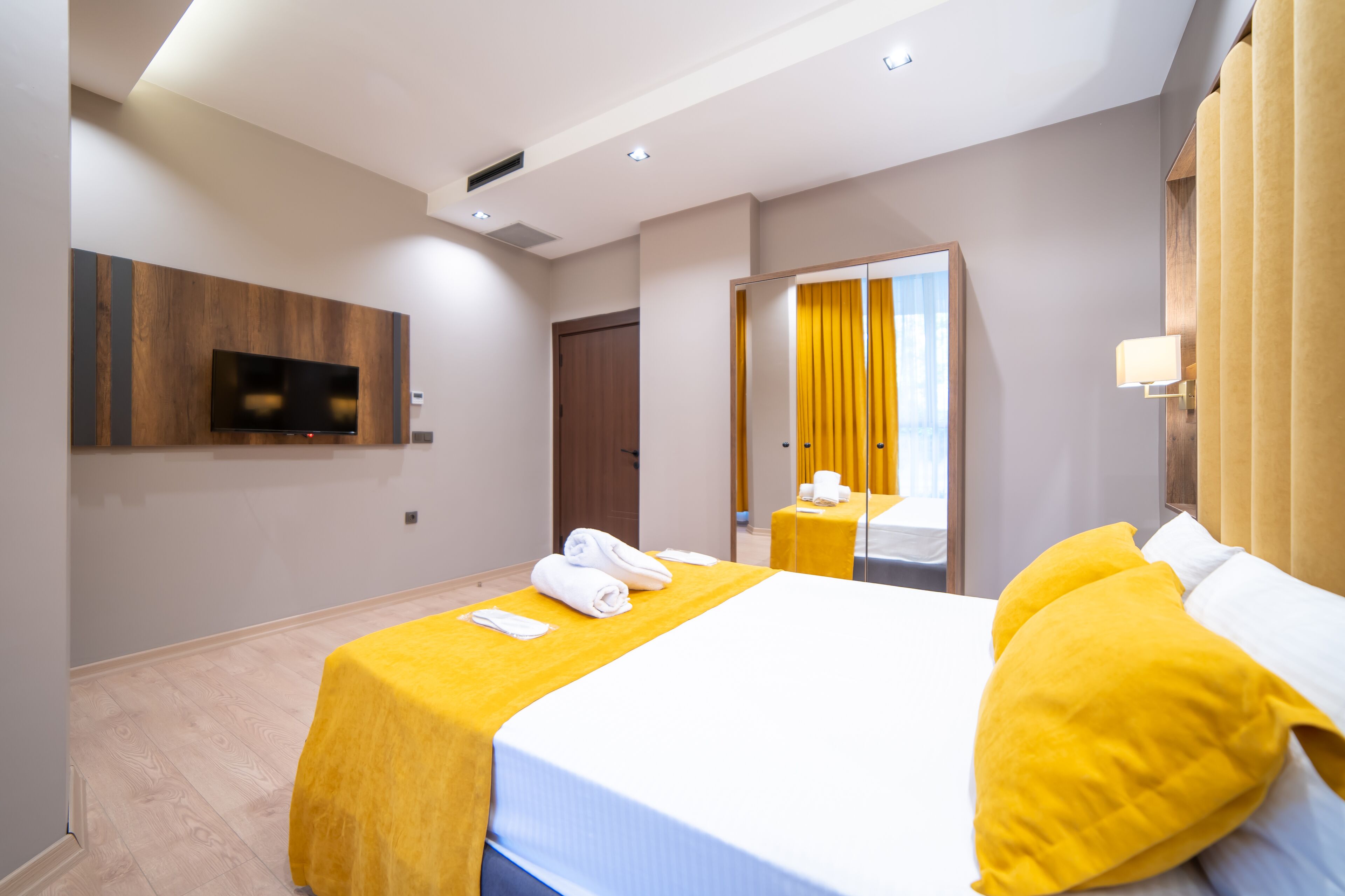 A modern hotel room with a bed, a TV mounted on the wall, a mirror, and a door leading to another room.