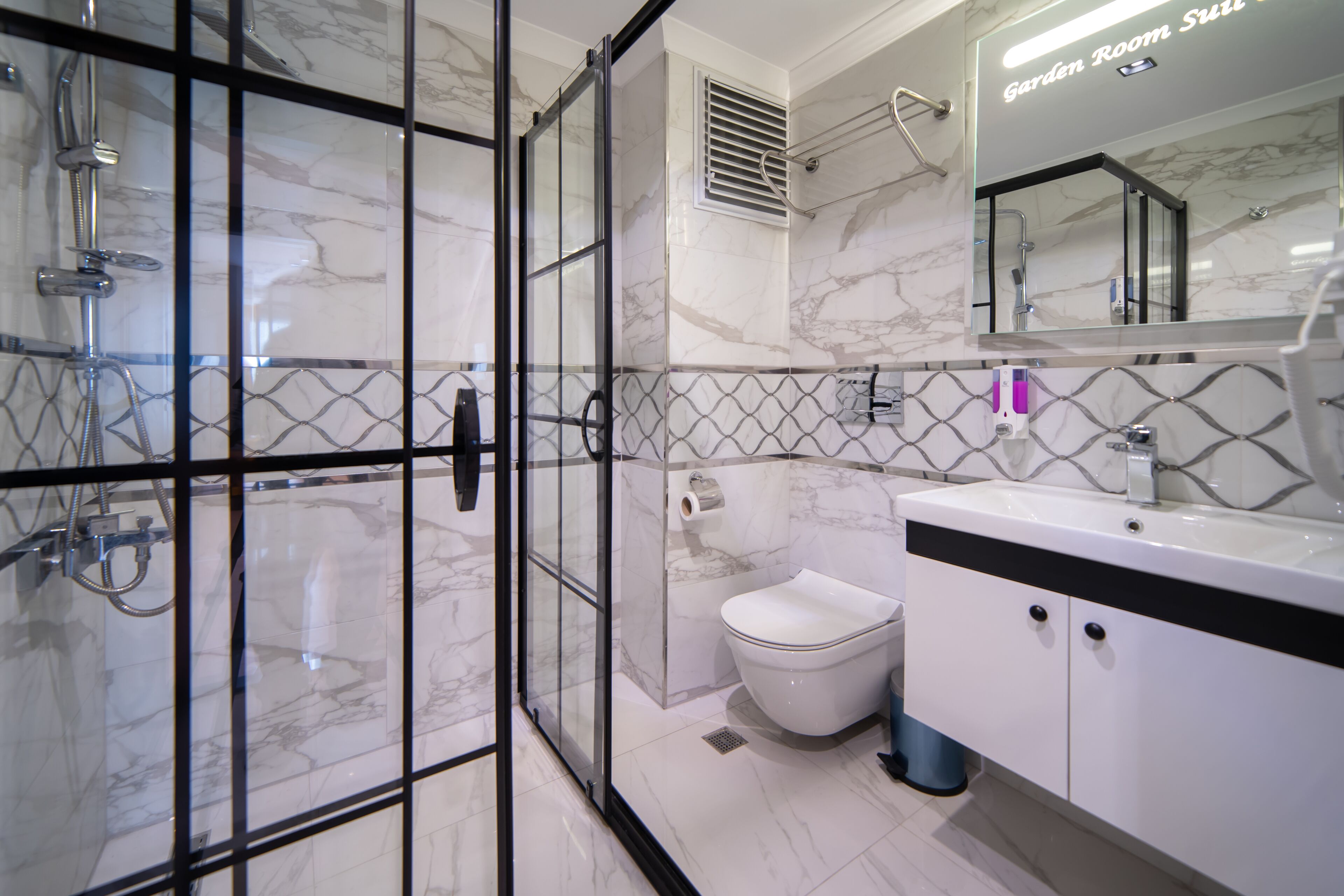 A modern bathroom with a glass-enclosed shower, a toilet, and a sink with a mirror above.