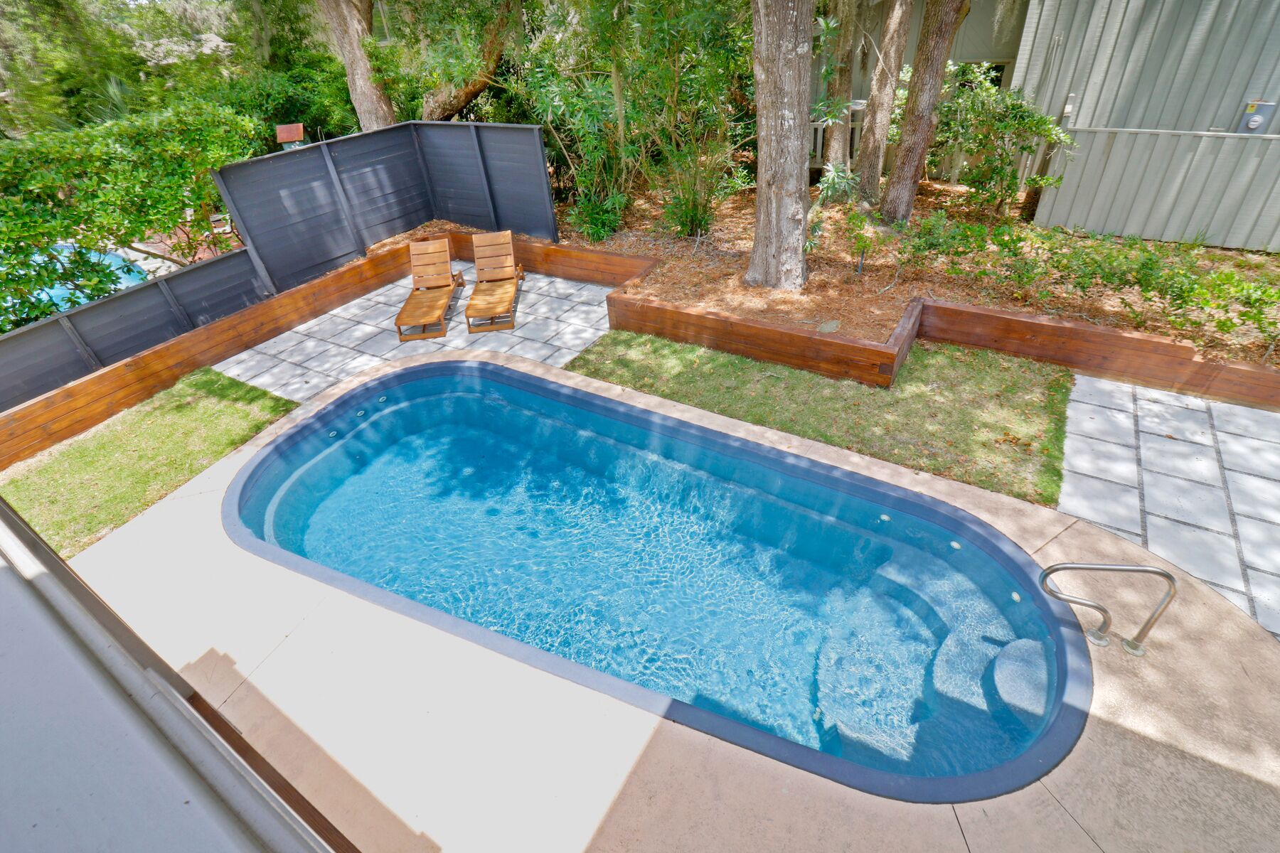 Una piscina rettangolare con idromassaggio integrato, circondata da un pontile in legno e da una zona verde.