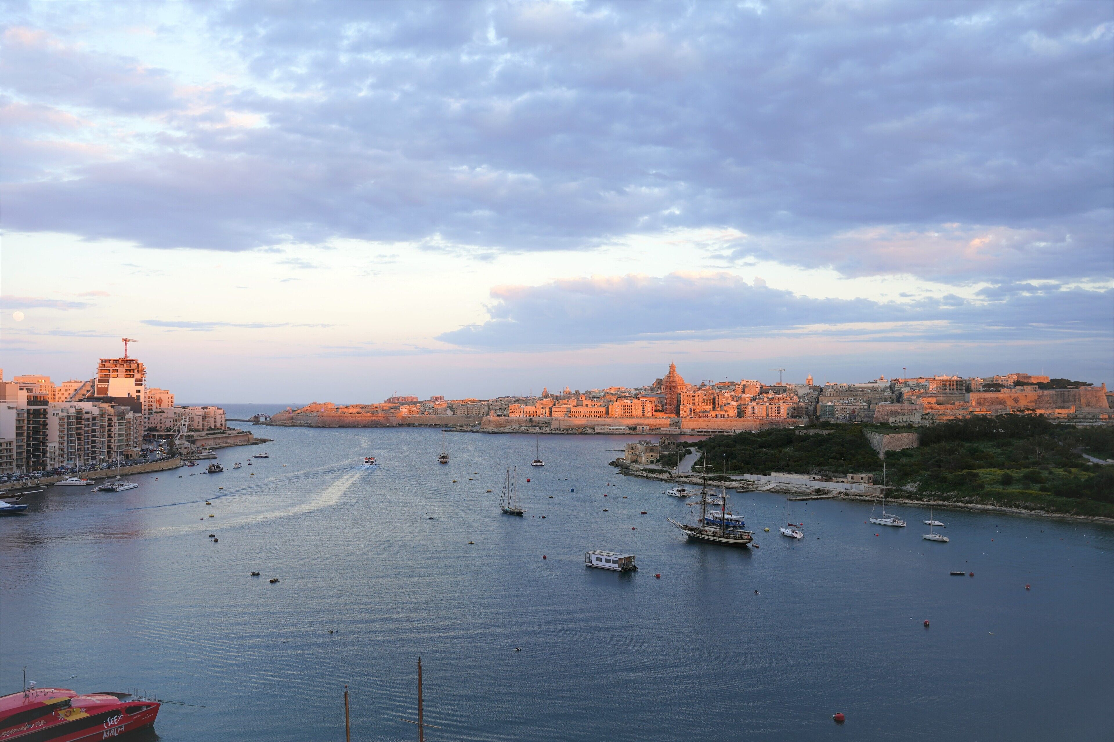 Un paisaje urbano costero con un puerto lleno de barcos, edificios históricos y una torre destacada.