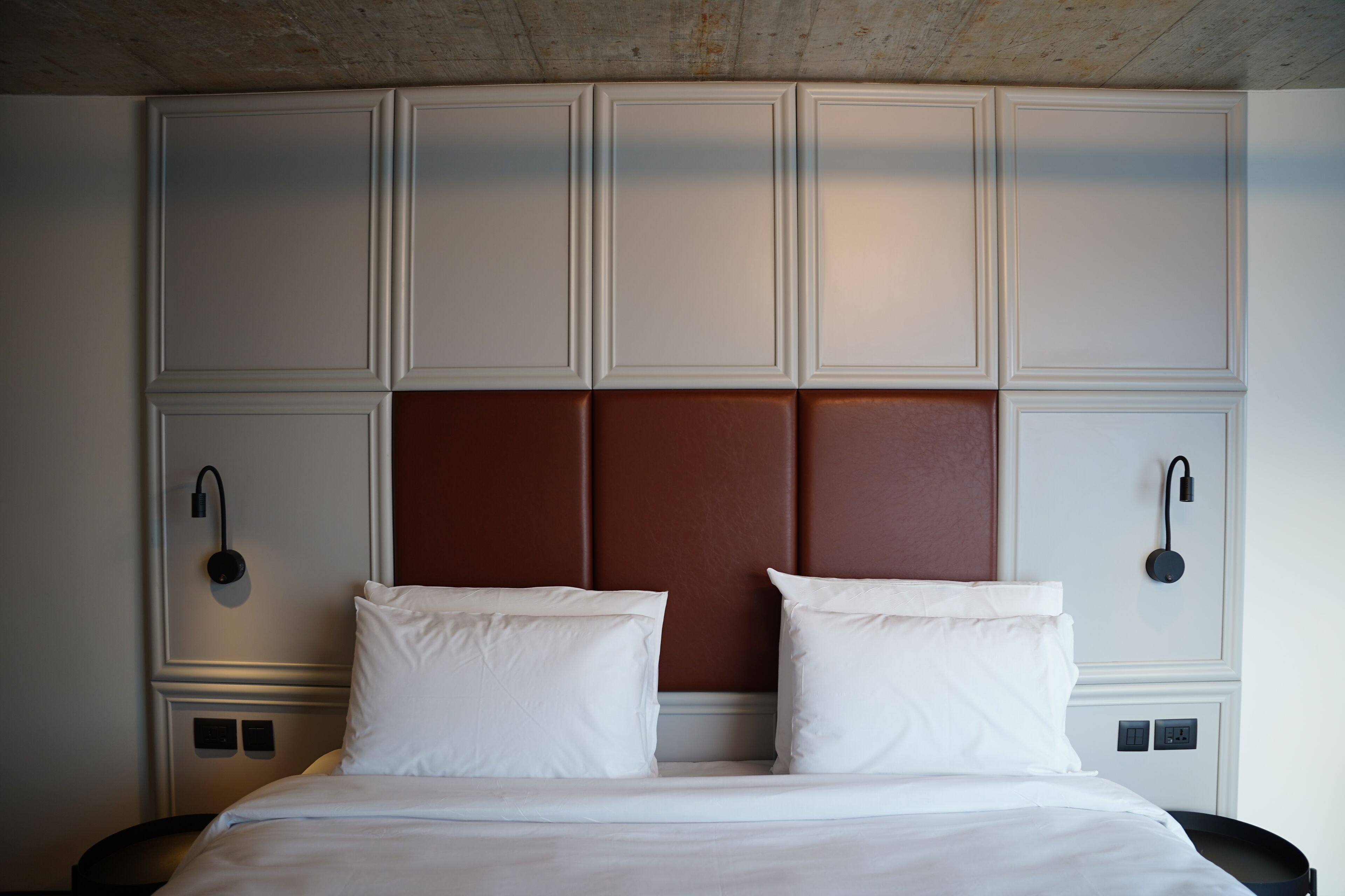 A hotel room with a large bed, a headboard with a brown panel, and two bedside tables with lamps.