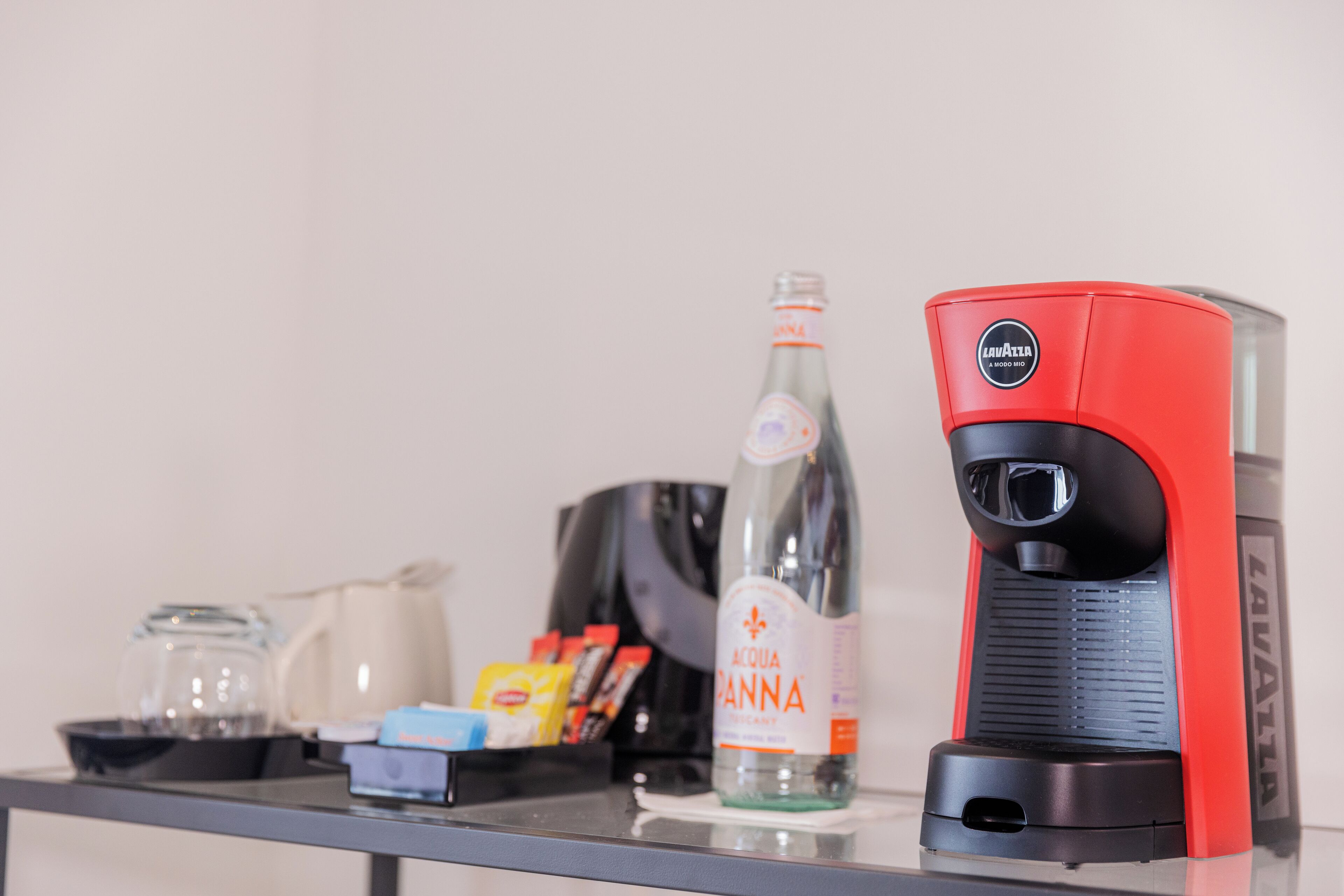 A coffee maker, a bottle of Acqua Panna water, a coffee pot, and some snacks on a table.