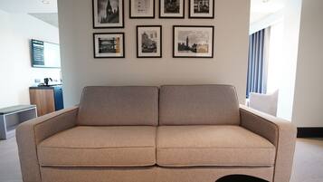 A modern living room with a beige sofa, a coffee table, and framed cityscape pictures on the wall.