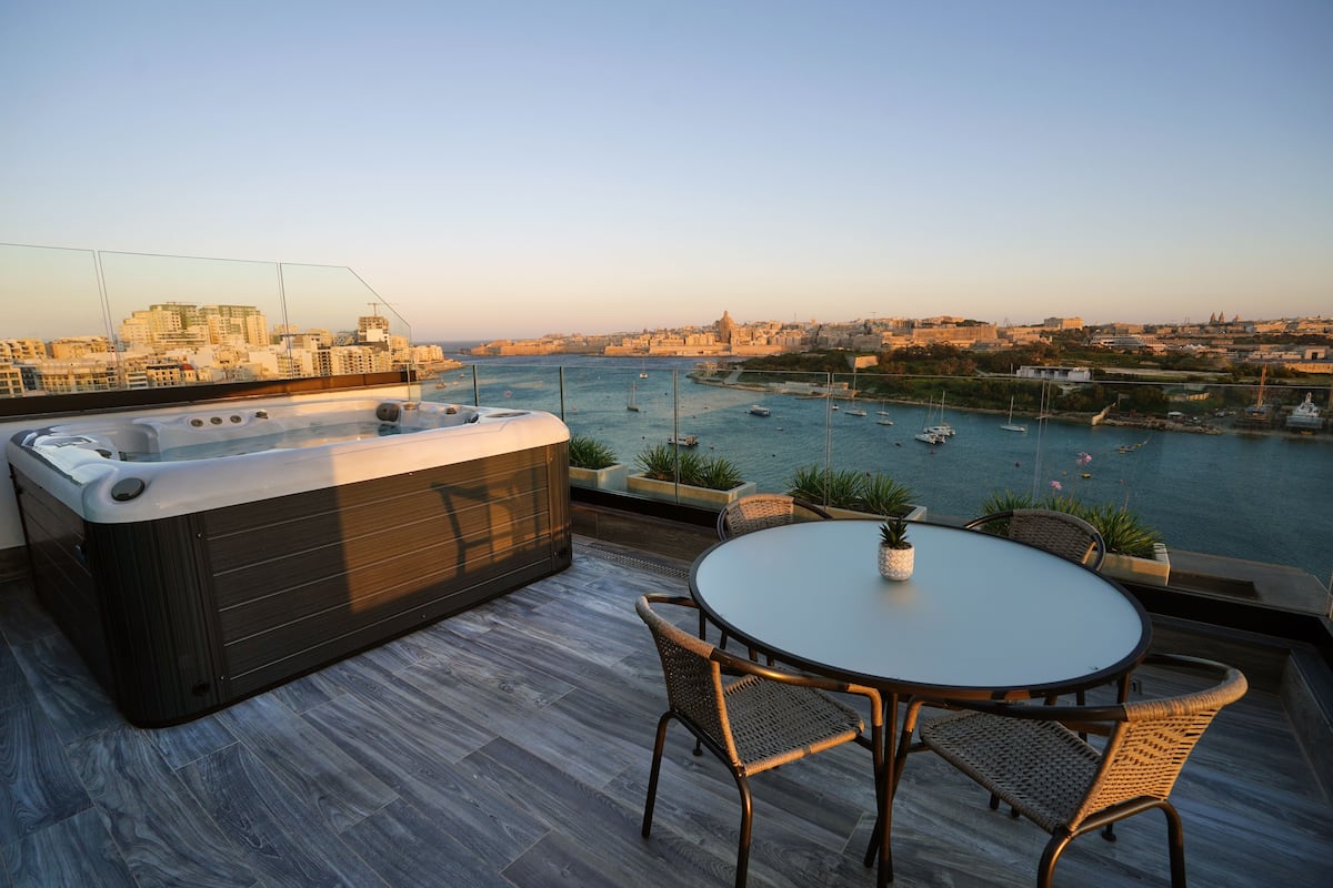 Una terraza en la azotea con un jacuzzi, una mesa redonda y sillas de mimbre.