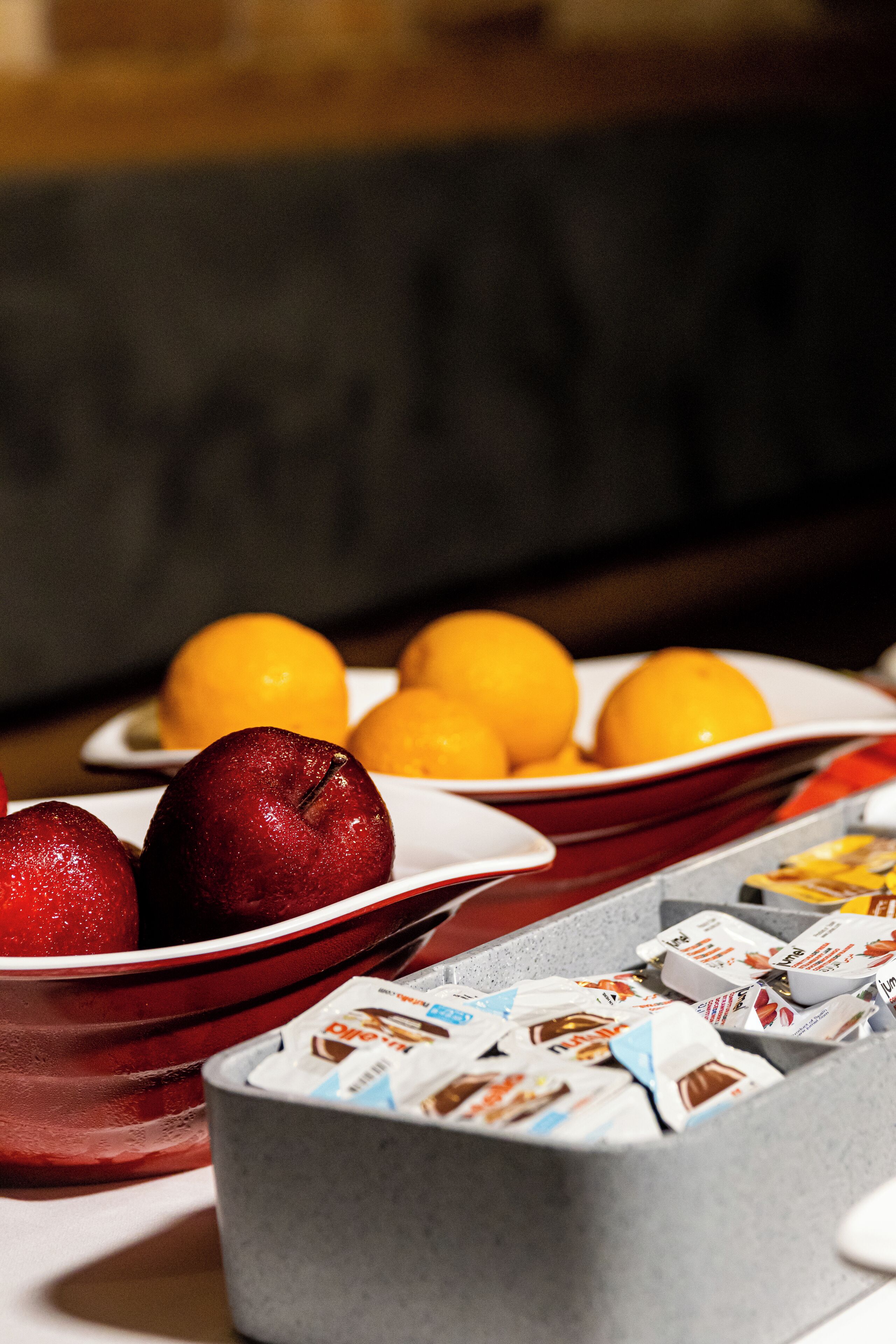 A breakfast buffet with plates of apples and oranges, and a container of coffee creamer packets.