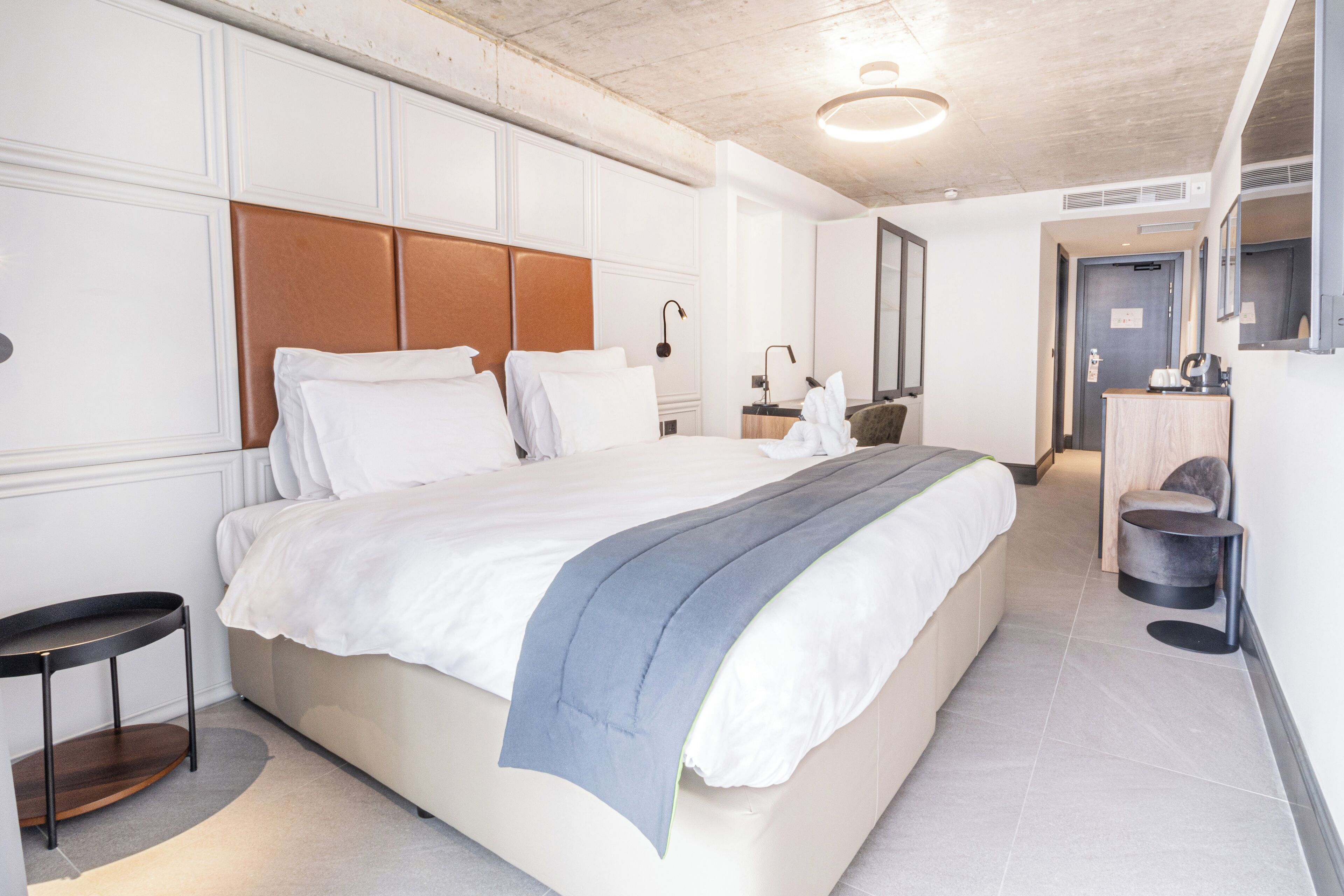 Une chambre d’hôtel moderne avec un grand lit, une table de chevet, un miroir et un petit coin salon.