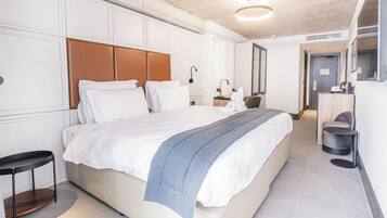 Una habitación de hotel moderna con una cama grande, una mesita de noche, un espejo y un pequeño espacio de descanso.