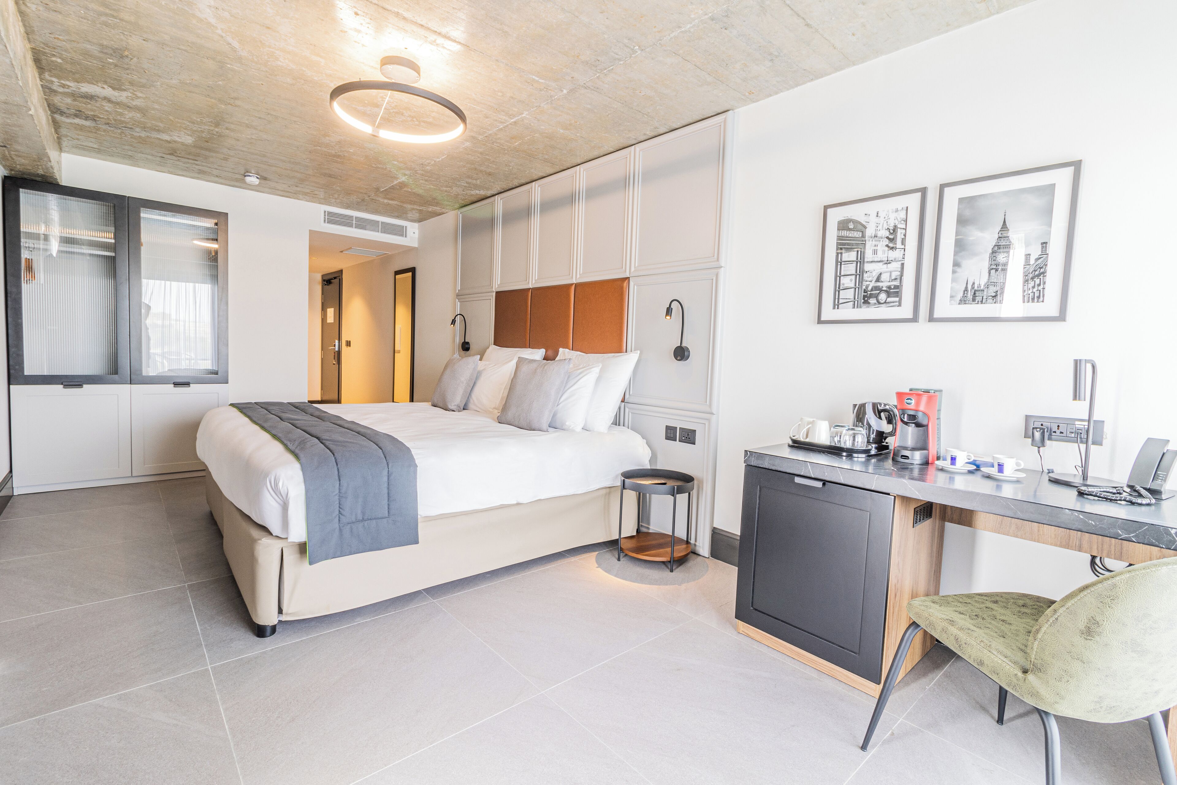 Een moderne hotelkamer met een bed, bureau, stoel en kunstwerk aan de muur.