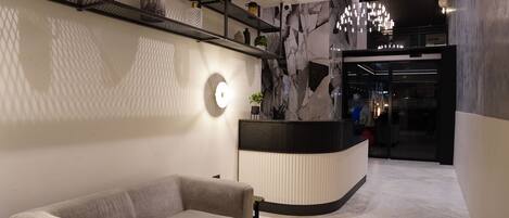 A modern lobby with a reception desk, a sofa, and a chandelier.