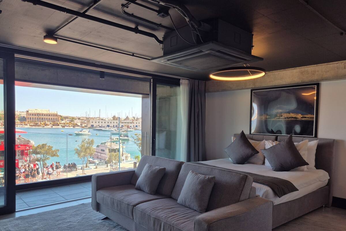 Una habitación de hotel moderna con una cama grande, un sofá y vista al puerto deportivo.