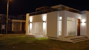 A modern two-story house with a flat roof, large windows, and a well-lit entrance.