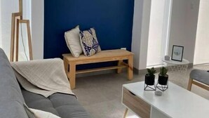 A modern living room with a blue accent wall, a grey sofa, a wooden bench, and a white coffee table with potted plants.