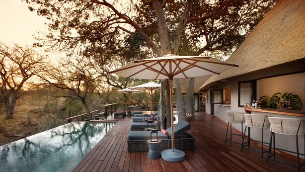 A wooden deck with outdoor seating and umbrellas, overlooking a pool and natural landscape. - Serondella Safari Lodge (Hoedspruit)