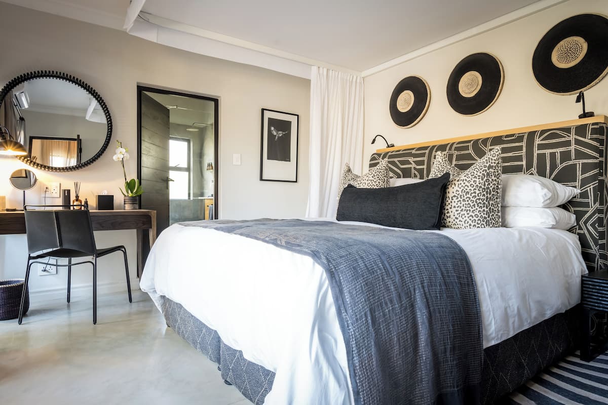A modern bedroom with a large bed, a desk, and a chair. There are decorative plates on the wall and a mirror above the bed.